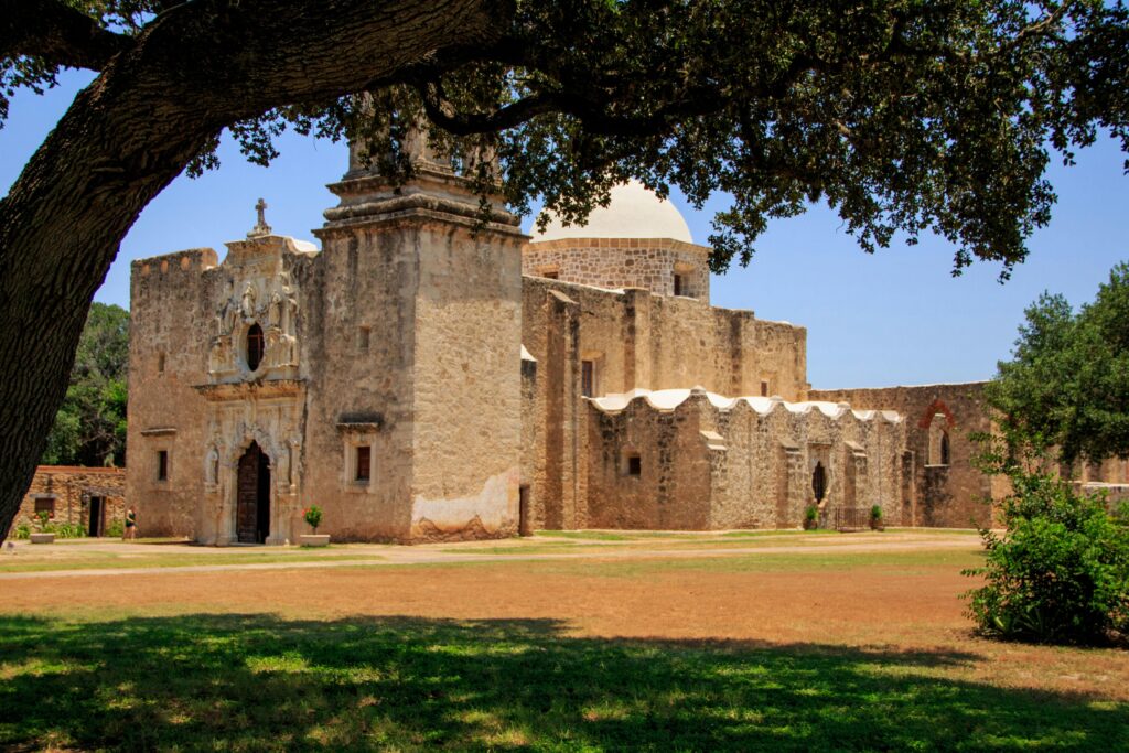 Statue of an old mission with lush trees in San Antonio, capturing historical architecture.