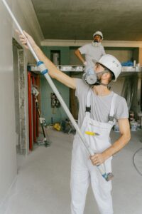 Two construction workers in safety gear are interior renovating, using a paint roller.